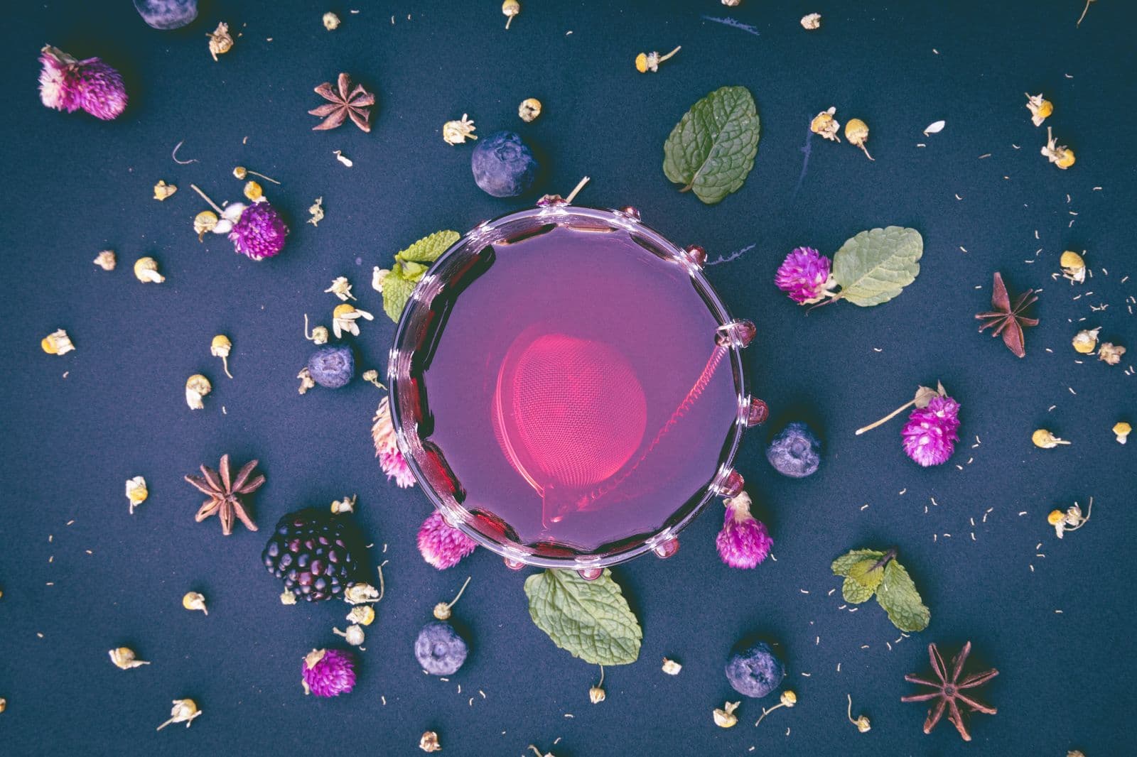 Colorful botanicals arranged around an herbal infusion